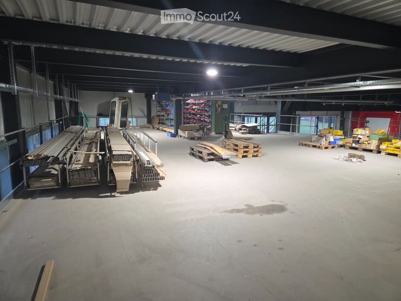 Empty warehouse with metal beams, concrete floor, storage shelves, and various items