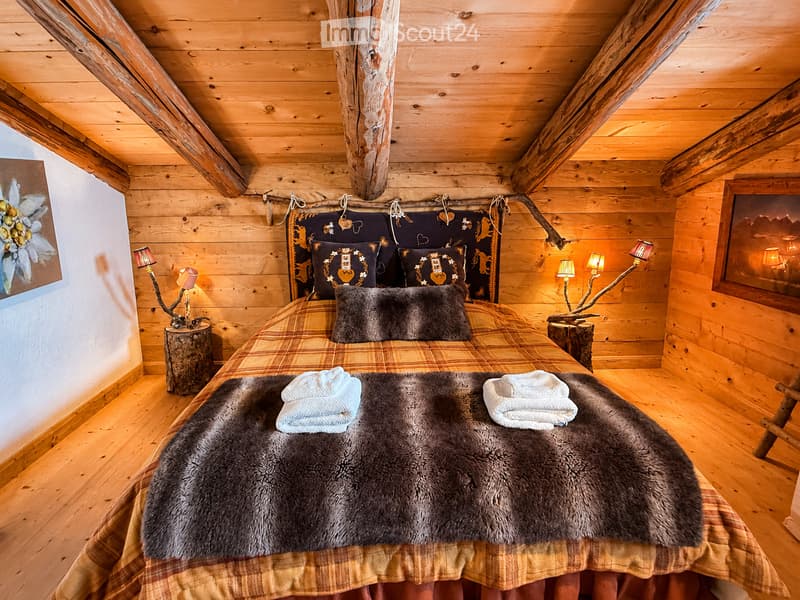 Cozy wooden bedroom with a large bed, fur throw, plaid blanket, decorative pillows, and two table lamps on wooden stumps.