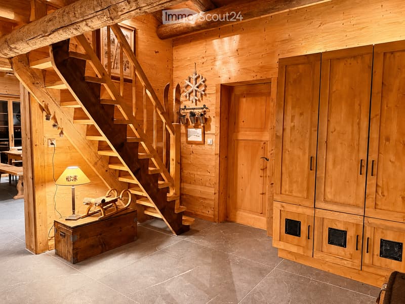 Cozy wooden hallway with a curved staircase, built-in wooden cabinets, and a small table with a lamp. The space features exposed wooden beams and a warm, inviting atmosphere.