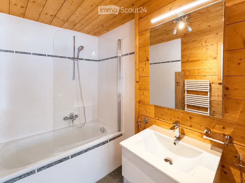 Modern bathroom with wooden walls and ceiling, featuring a bathtub, sink, mirror, and radiator.