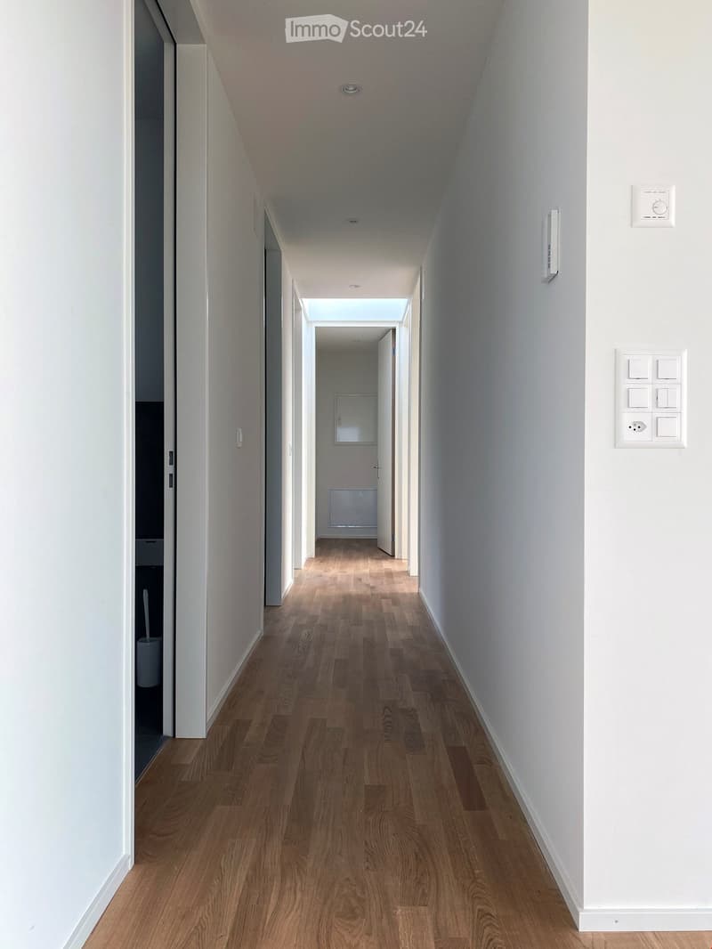 Empty hallway with wooden floors, white walls, and ceiling lights