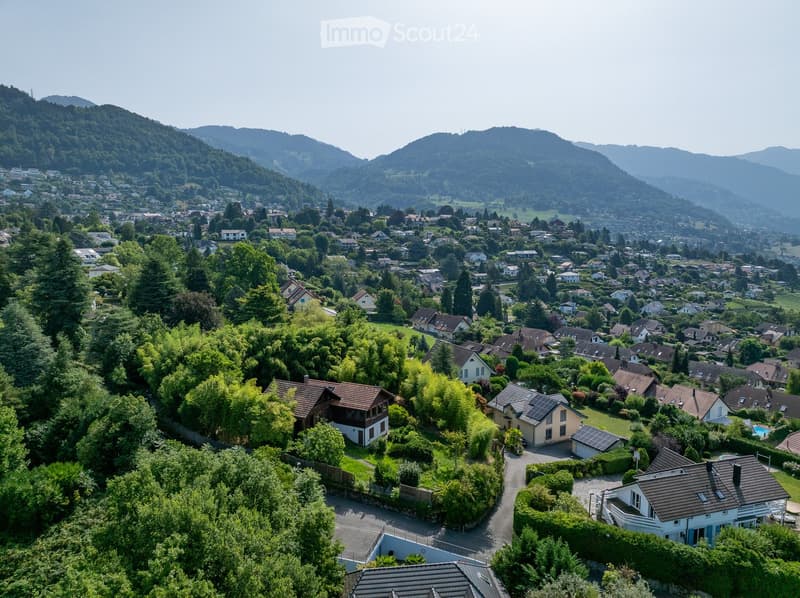 Aerial view of houses in a hilly landscape with mountains in the background.