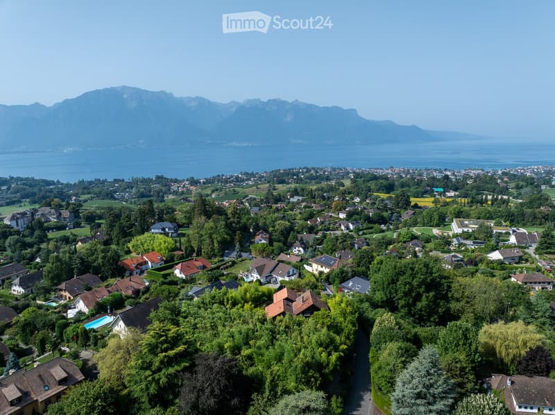 Cluster of residential houses on hillside, one house with pool, mountainous area and sea in the background