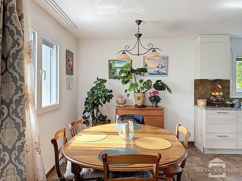 Dining room with wooden table, chairs, plants, and a chandelier