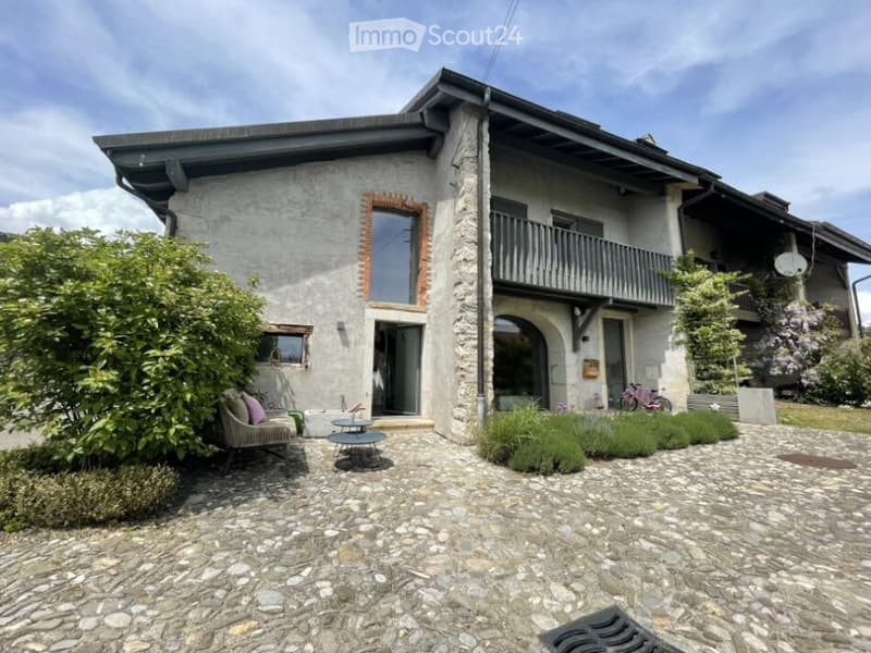 Two-story stone house with a balcony, stone-paved courtyard, outdoor seating area, and garden.
