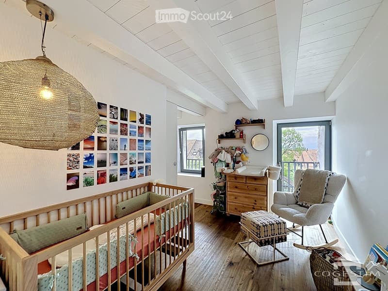 Bright, airy bedroom with wooden crib, rocking chair, and large window overlooking a balcony.