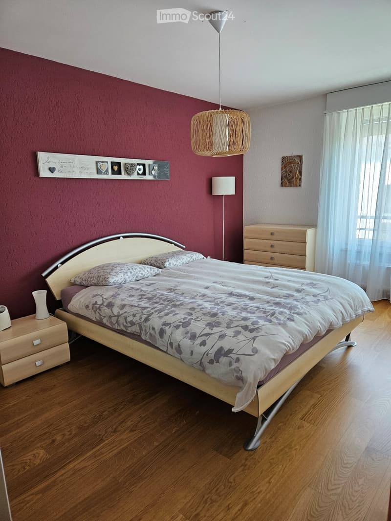large bed, red wall, wooden floor, wooden nightstands, wooden cabinet, standing lamp, art frame, white curtains