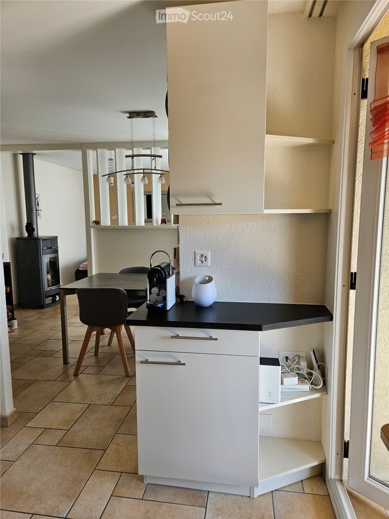 Modern kitchen with white cabinetry, a black countertop, an electric kettle, and dining furniture.