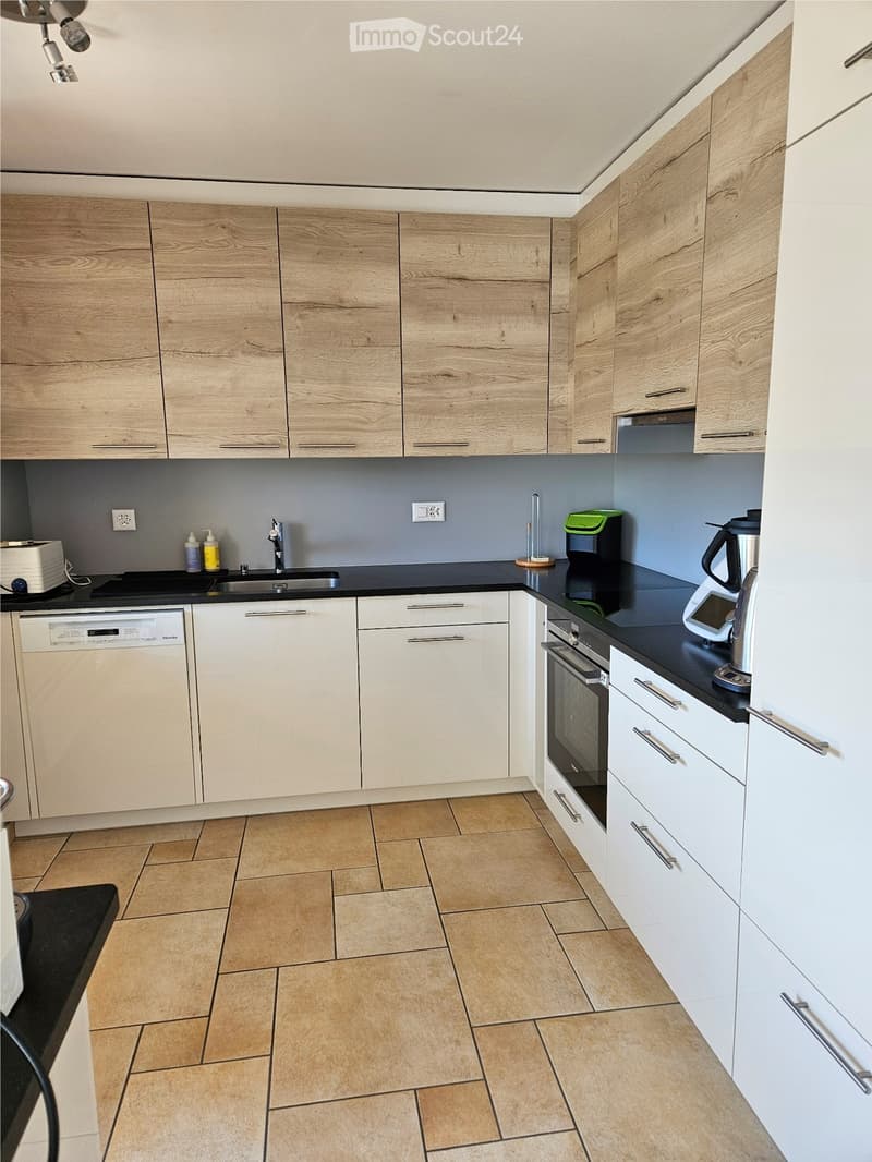 Wooden cabinets, black countertops, dishwasher, stainless steel appliances, tiled floor