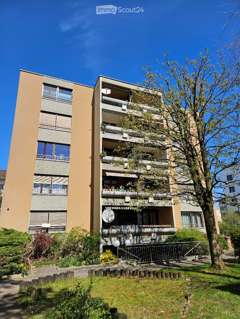 multi-story building, balconies, greenery in front, satellite dish