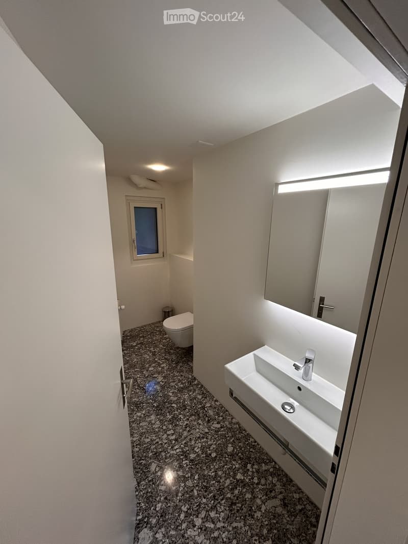 Bathroom with white walls, granite floor, white sink, mirror, toilet, small window