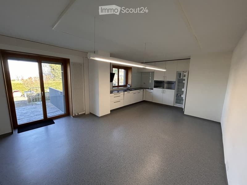 empty room, white walls, gray floor, sliding glass door, kitchen with white cabinets, appliances, and a sink