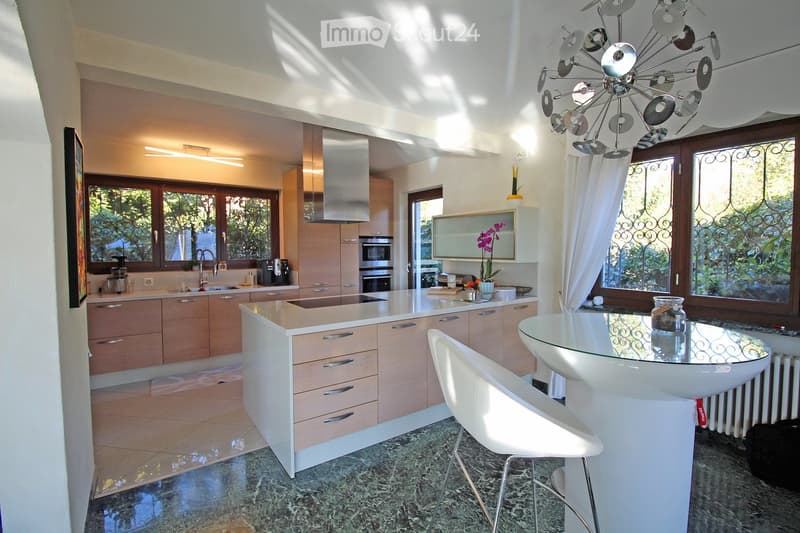 modern kitchen with white countertops, wooden cabinets, glass table, white chairs, chandelier, windows, appliances