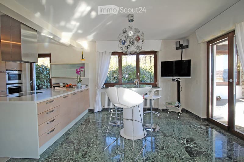 modern kitchen with marble floor, white countertops, wooden cabinets, built-in oven, microwave, refrigerator, island with bar stools, chandelier, TV, and glass doors leading to a patio