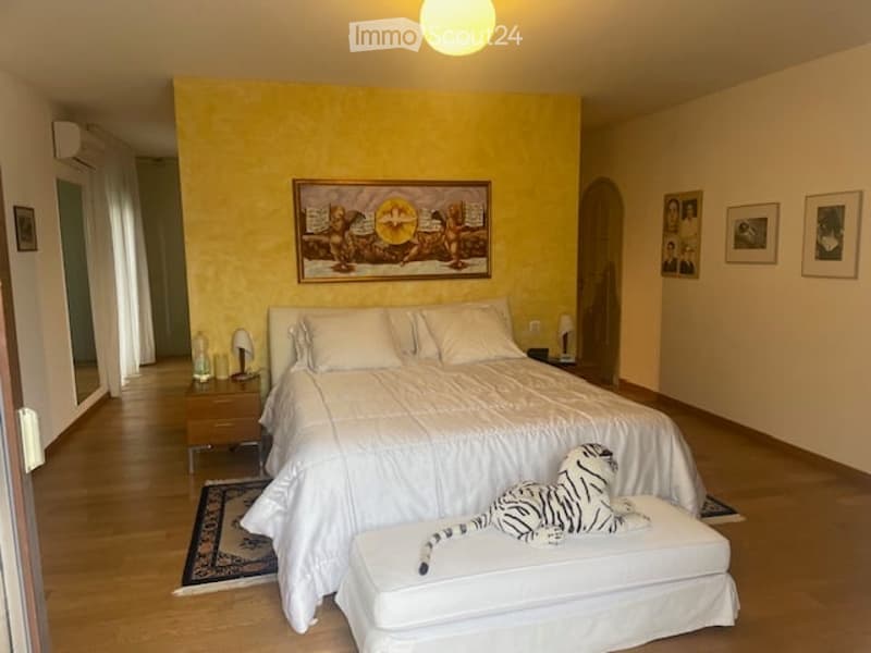 A bedroom with a bed, nightstands, a tiger plush toy, a rug, a painting, and a yellow wall