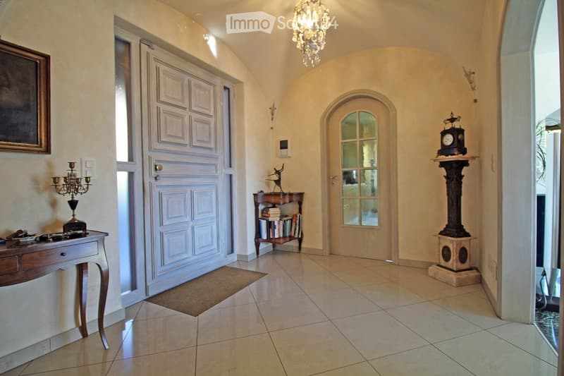 Entrance hall with white tiles, white doors, chandelier, table with candelabra, clock, books on a shelf, picture frame