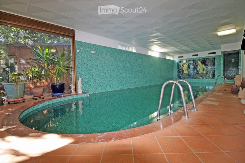 Indoor swimming pool with green tiles, handrails, and plants