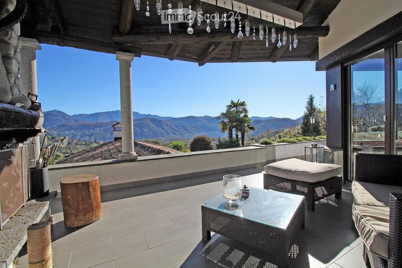 Outdoor terrace with a view of the mountains, a fireplace, a glass table, and wicker furniture.