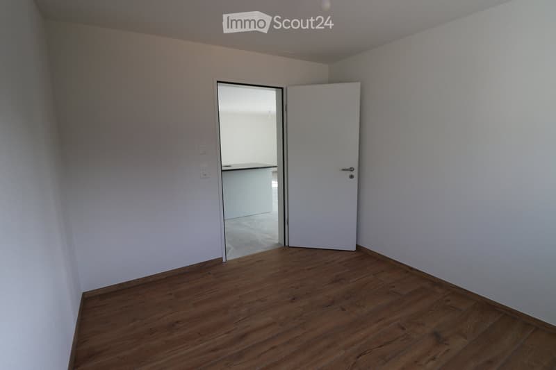 Empty room with white walls, wooden floor, open door leading to another room