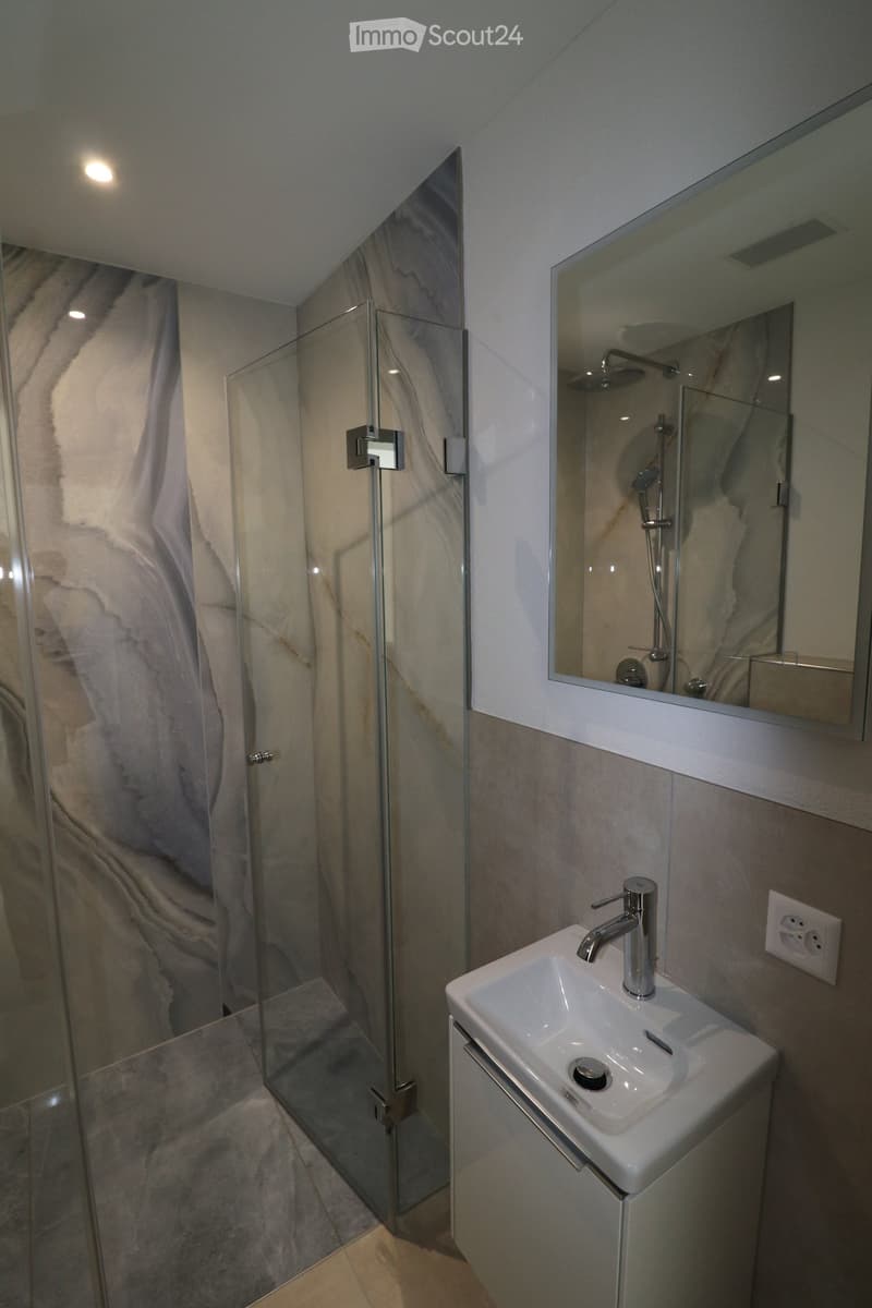 modern bathroom with glass shower, white sink, mirror, marble wall