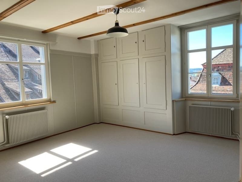 empty room, white walls, white ceiling, white radiators, large windows, wooden beams