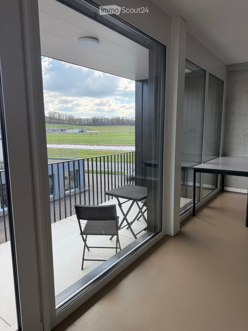 Balcony with table and chairs, large windows, view of the field