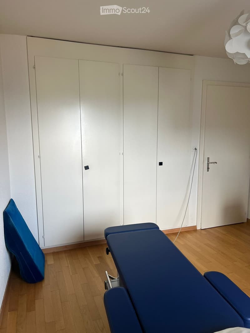 empty room with white wardrobe, blue massage table and bed, wooden floor
