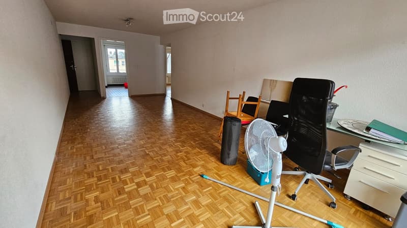 empty room, wooden floor, white walls, office chair, desk, fan, storage boxes, radiators