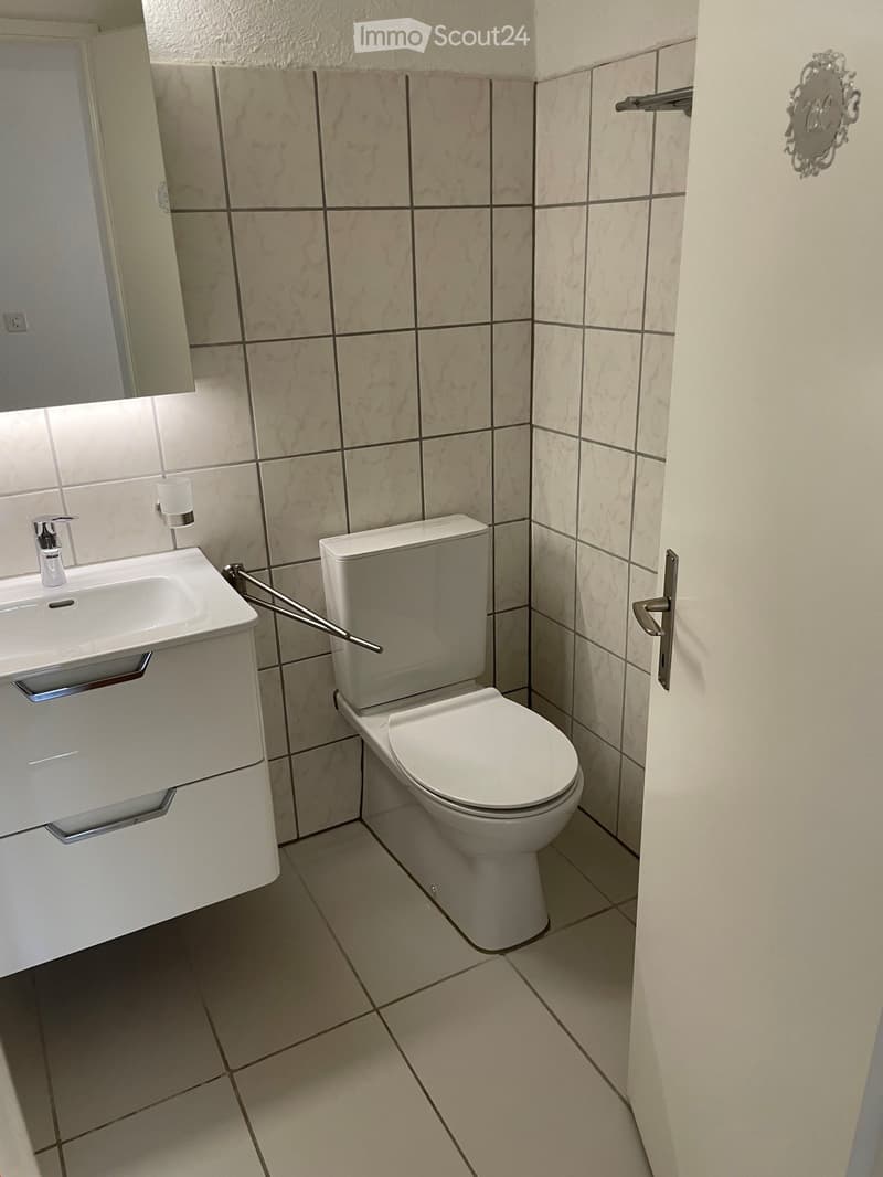 small bathroom with white tiles, white sink, white toilet, white cabinet, mirror, power outlet