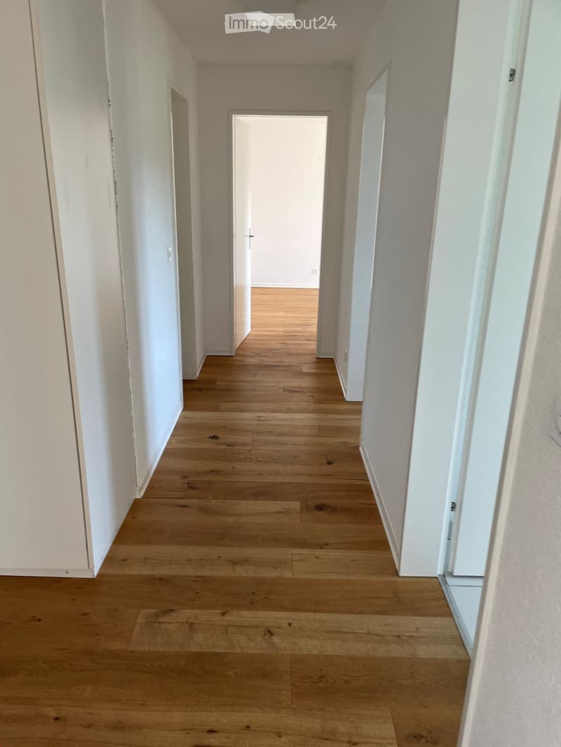 Empty hallway with wooden floor, white walls, and doors on both sides.