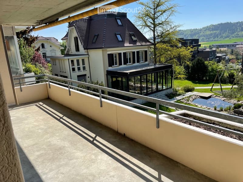 Balcony with metal railing, concrete floor, view of a house and garden