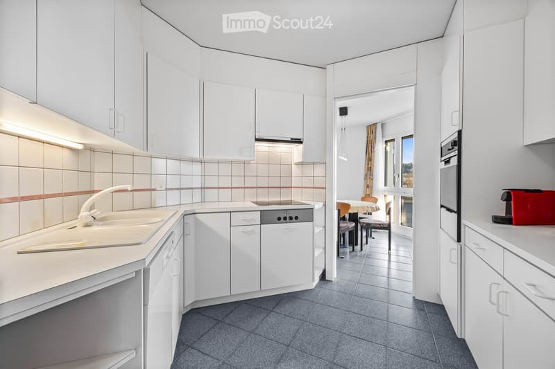 modern kitchen with white cabinets, tiled walls, stainless steel appliances, dishwasher, washing machine, and a dining area with a table and chairs