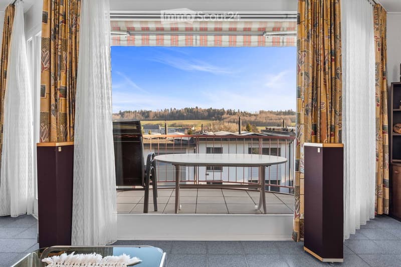 Balcony with table and chairs, large window with curtains, view of the landscape