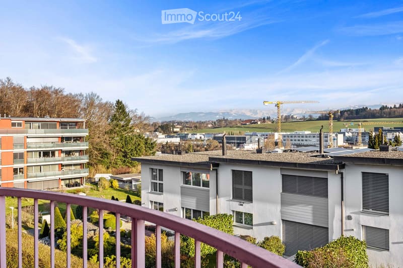 Balcony, white building, orange building, green trees, green grass, solar panels, mountains in the distance