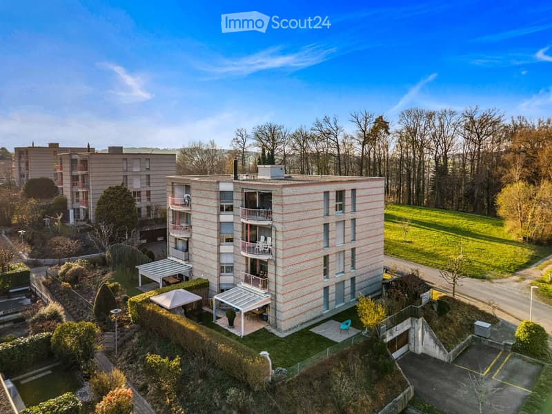 Apartment building with multiple balconies, covered parking, and a green lawn area.