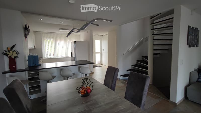 Dining room: Large wooden dining table, four chairs, refrigerator, white kitchen, white staircase, fireplace