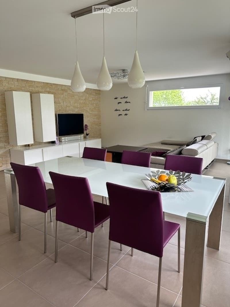 Dining room with a white table, purple chairs, a TV, a couch, and a brick wall