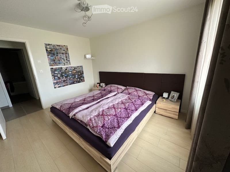 Bedroom with wooden bed, purple bedding, wooden nightstands, picture frames, and a chandelier on the ceiling.