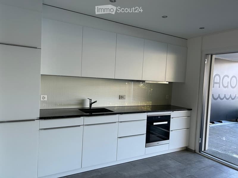 White kitchen with black countertops, modern cabinets, stainless steel sink, oven, dishwasher, power outlets.