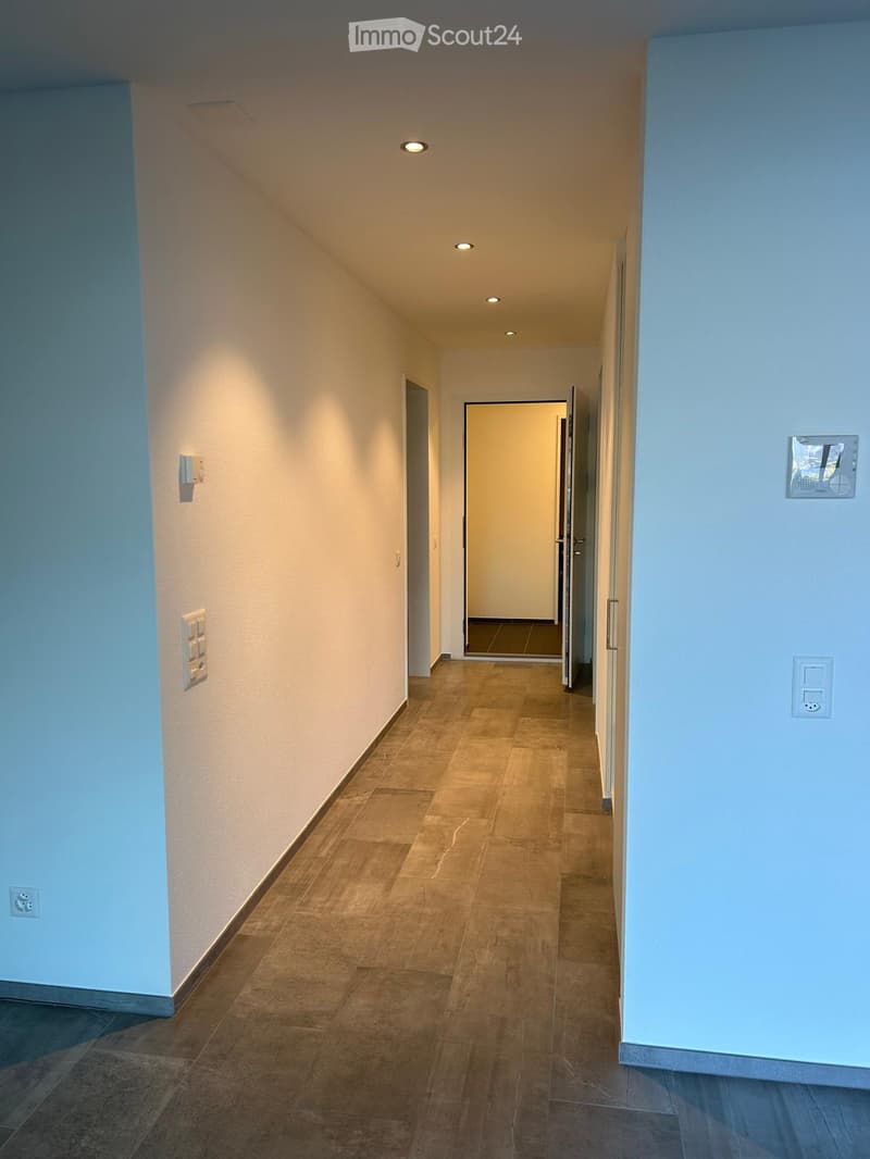 Empty hallway, white walls, tiled flooring, ceiling lights, an open door, power outlets, and a light switch