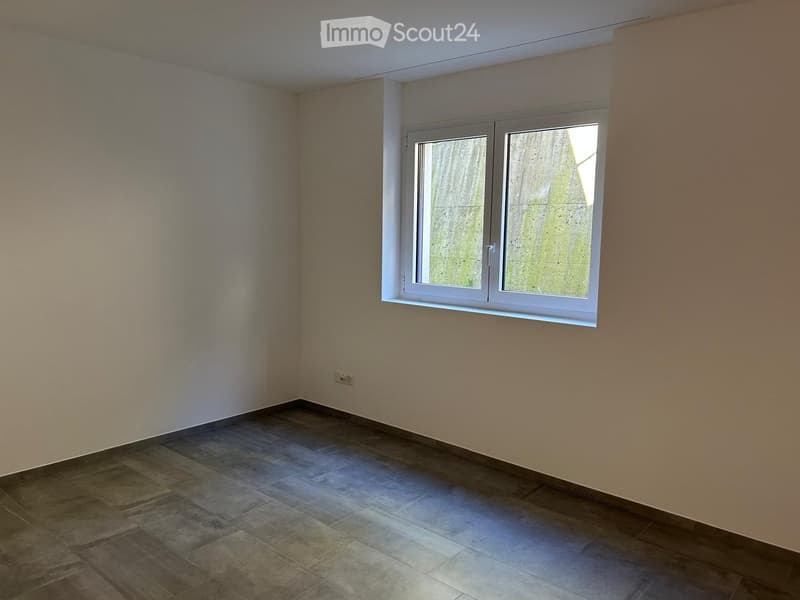 empty room with white walls, wooden floor, one window, power outlet