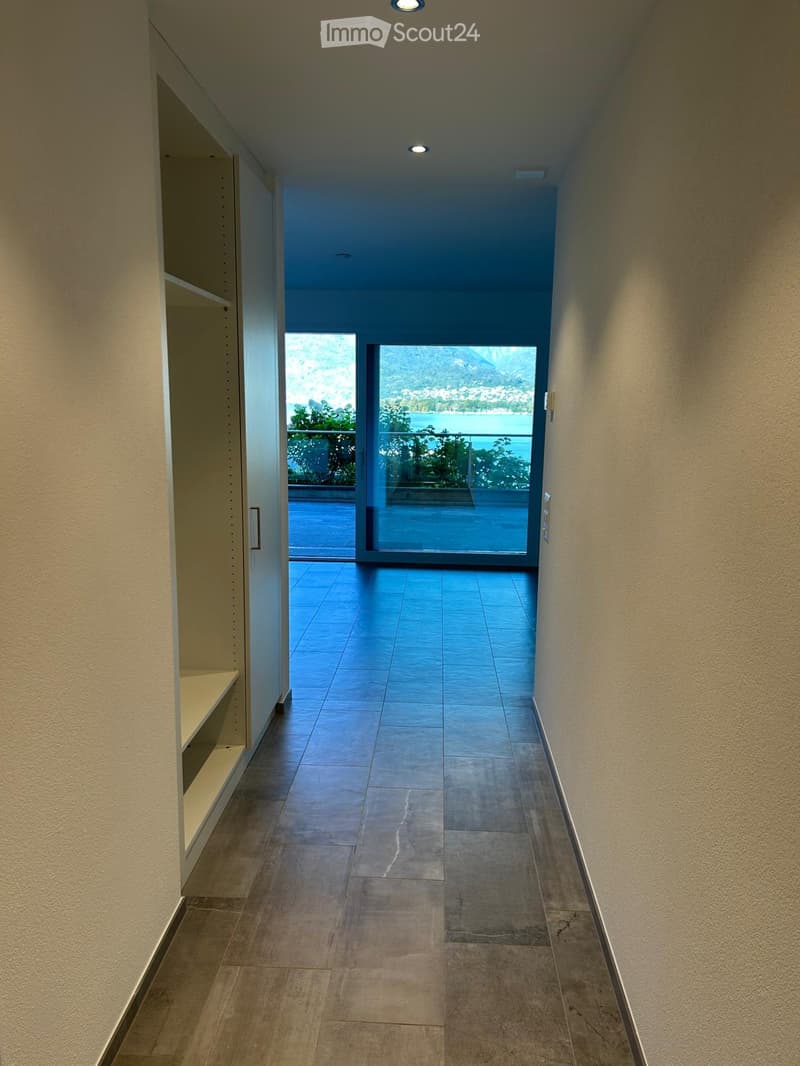 empty hallway, wooden floor, sliding glass door, glass door leading to balcony, balcony with railing, lake view, white walls