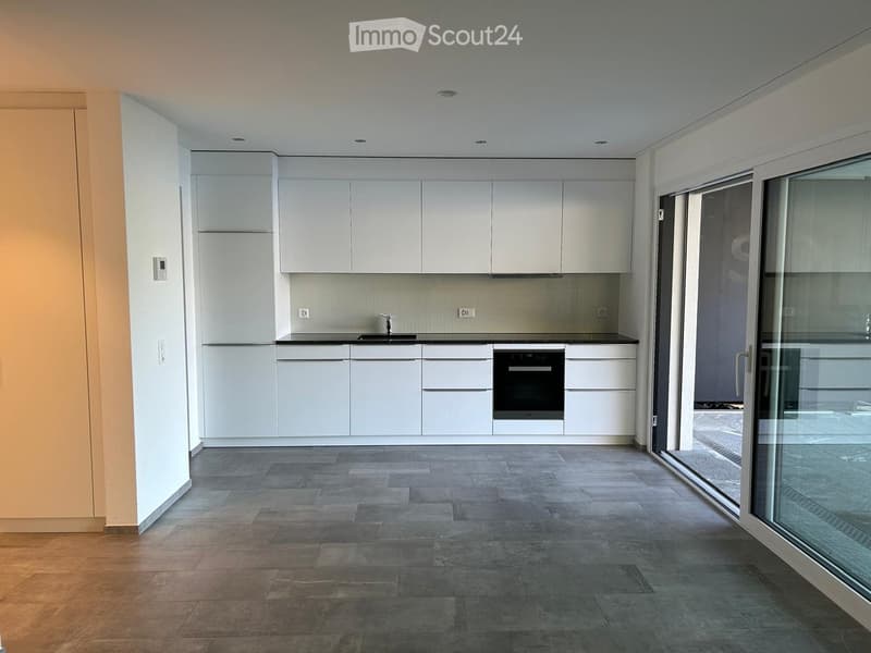 Empty kitchen with white cabinets, grey floor, black countertops, black oven, sliding glass door leading to a paved area