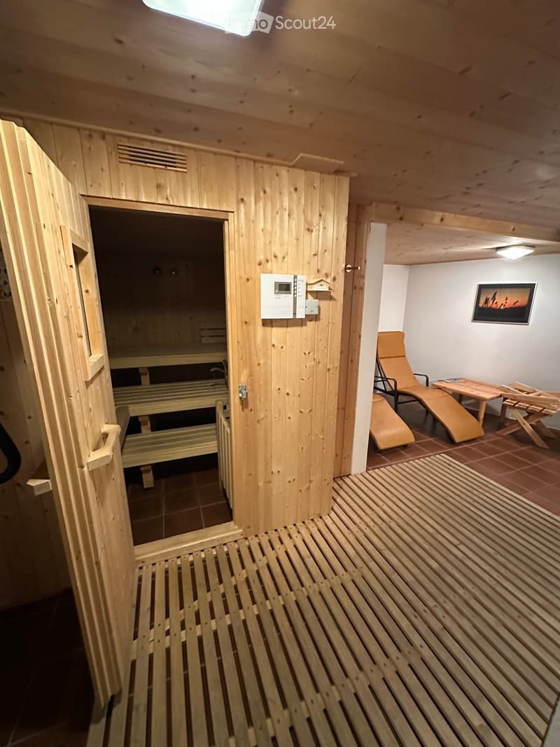 Wooden sauna with benches, wooden chair, wooden table, rug, and painting on the wall.
