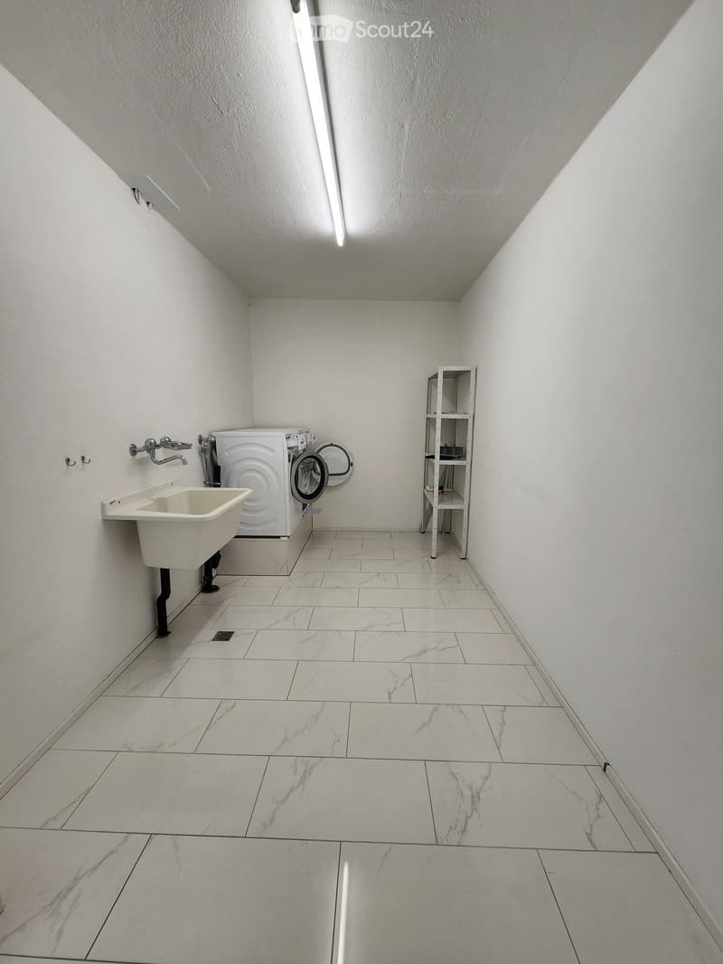small room, white tiled floor, white walls, washing machine, sink, no windows