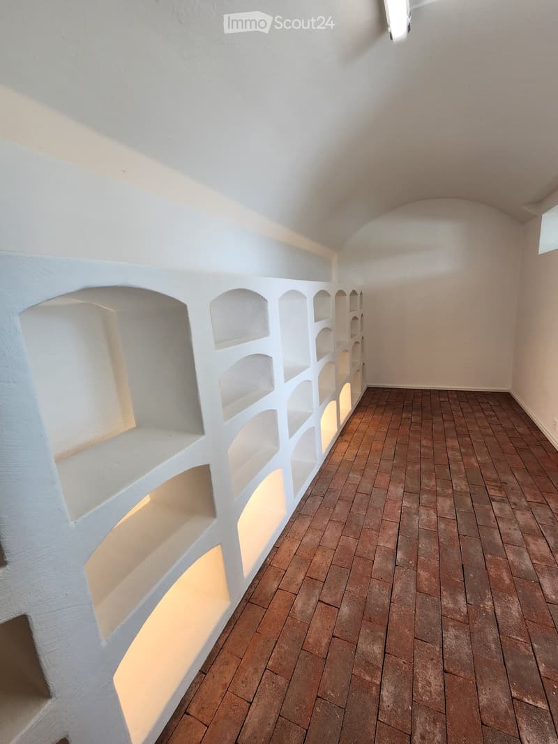 Room with white walls, arched alcoves, and brown brick flooring. Dimly lit with recessed lighting.