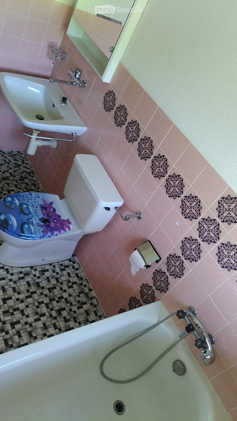 Bathroom with pink tiles, a bathtub, toilet, sink, and a decorative toilet seat cover with flowers.