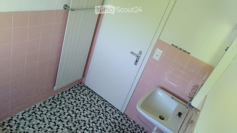 Bathroom with pink tiled walls, black and white checkered floor, white sink, and a door with a silver handle.