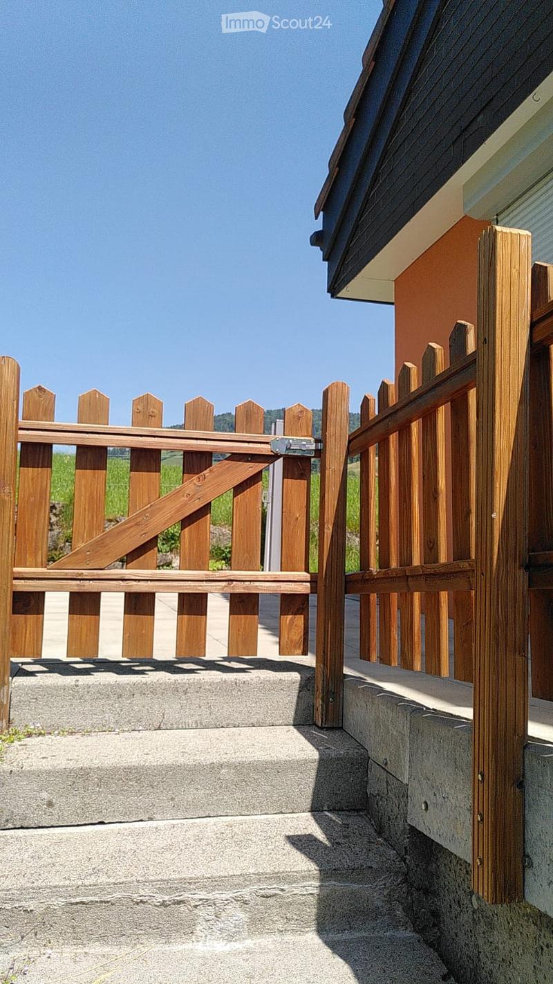 Wooden fence with a gate, concrete steps, and a view of a green field and distant hills.