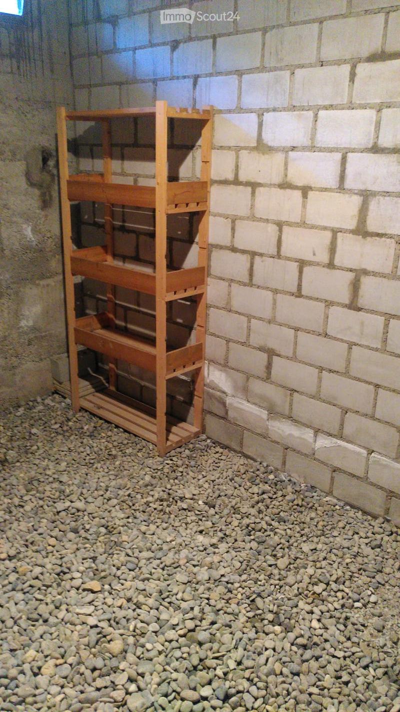 Empty room with exposed brick walls and a wooden shelving unit, covered in small rocks on the floor.